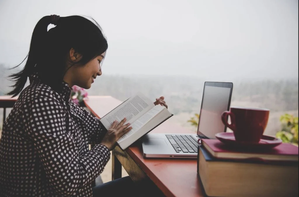student reading book with laptop and coffee
