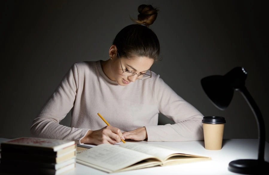 Student writing notes under a desk lamp